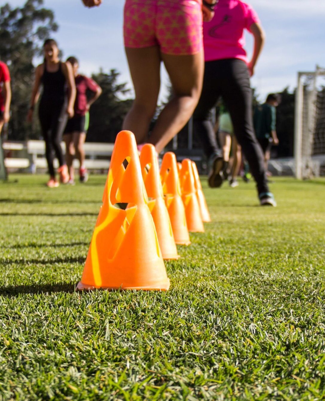 Dynamic soccer training session with teenagers practicing agility using orange cones on grass field.