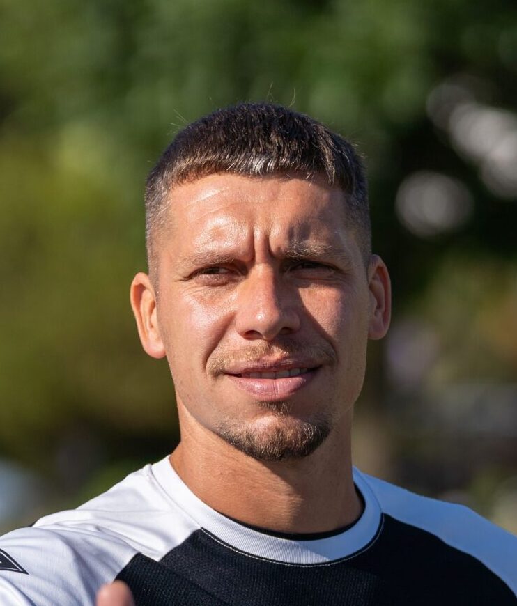 A soccer player in training gear gives a thumbs up in a sunny outdoor setting.