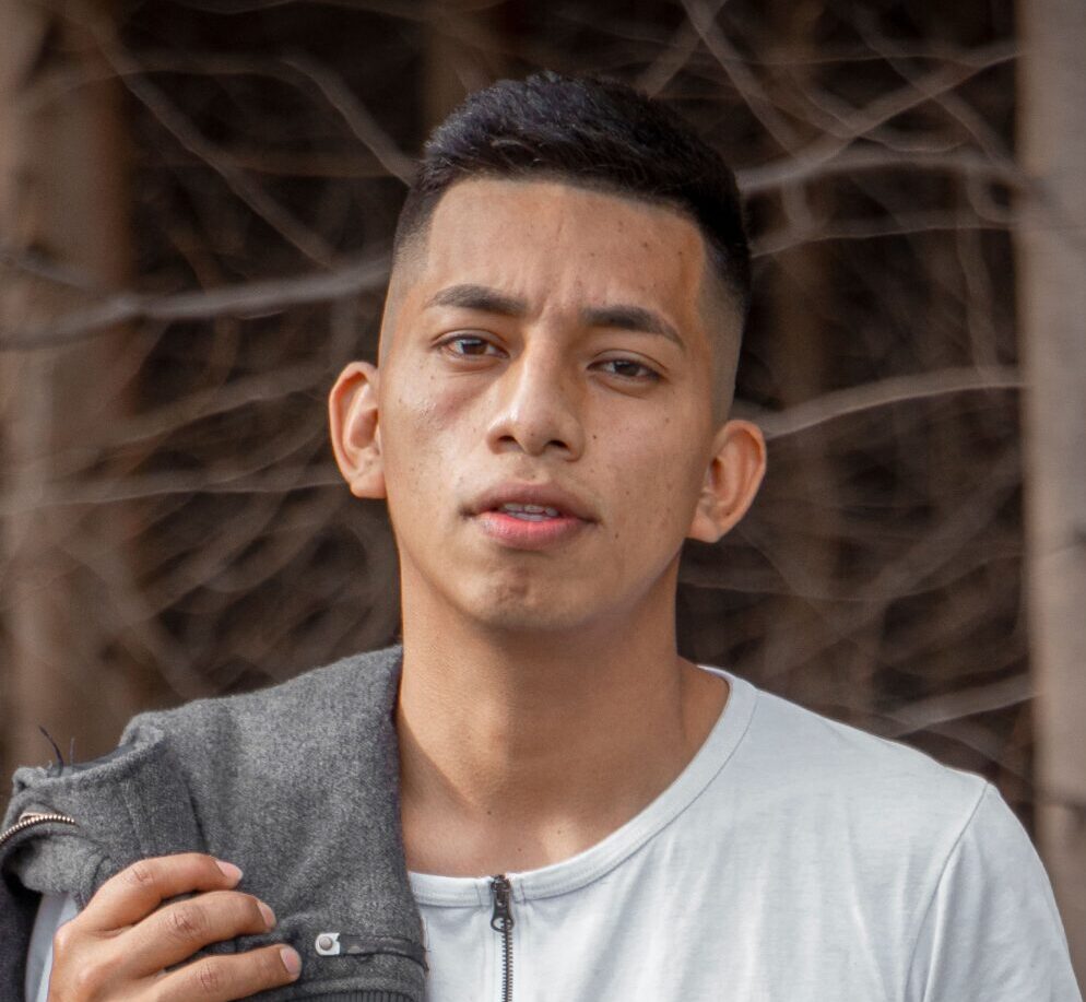 Young man posing outside with a casual outfit, holding a jacket over his shoulder.